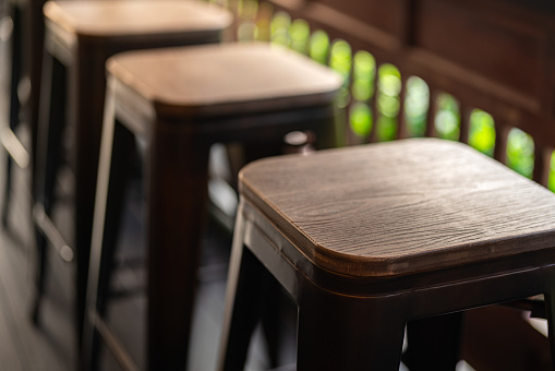 Row of tall wooden and iron retro style seats at the coffee counter bar. Furniture object photo, close-up and selective focus at the seat's part.