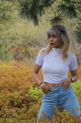 A Filipino model in a public park as Spring colors are bursting. She is wearing medium length multi colored hair, makeup, a necklace, white t shirt, jeans and a watch and bracelets.