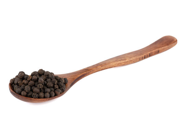 Wooden spoon with black pepper peas isolated on white background. Food seasonings.
