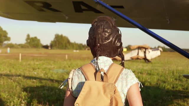 Young adventurous woman pilot walking to old airplane at summer sunset. Freedom and feminism concept. Breathtaking adventure in the air. Proffesional captain girl preparing for flight and skydiving