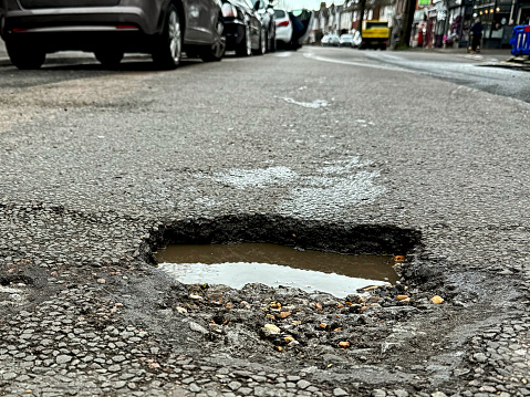 A deep, water filled pothole in a shopping street in Eastbourne, East Sussex, UK.