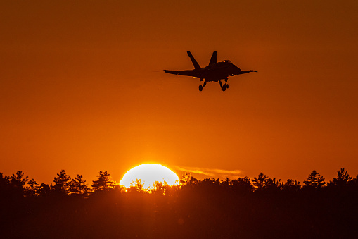 Gatineau, QC – September 15, 2023: A Royal Canadian Air Force FA-18 is silhouetted against an orange sky as it flies above the treeline with the setting sun in the background. The aircraft was part of the RCAF FA-18 Demo Team and is seen taking off with the afterburner lit. The performance was part of the AeroGatineau 2023 Airshow.