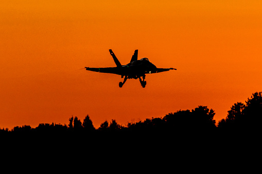 Gatineau, QC – September 15, 2023: A Royal Canadian Air Force FA-18 is silhouetted against an orange sky as it flies above the treeline with the setting sun in the background. The aircraft was part of the RCAF FA-18 Demo Team and is seen taking off with the afterburner lit. The performance was part of the AeroGatineau 2023 Airshow.