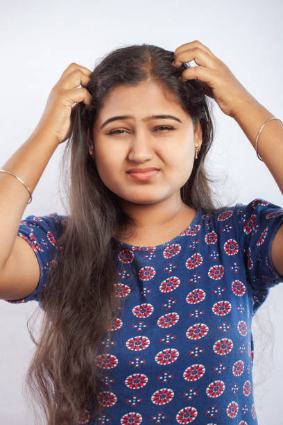 head lice, indian women scratching her head due to head louse and dandruff standing against a white background stock photo