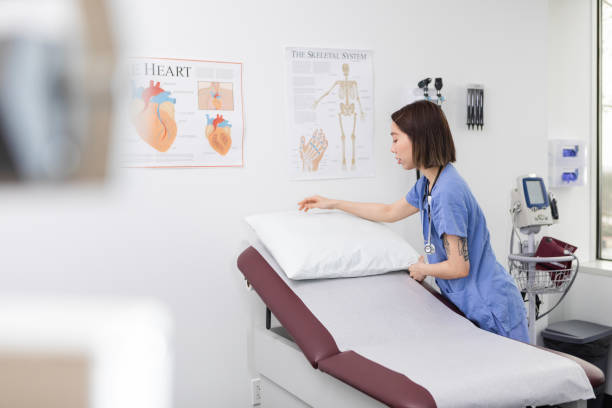 The young adult female nursing student arranges the pillow as she prepares the examination room for a new patient.