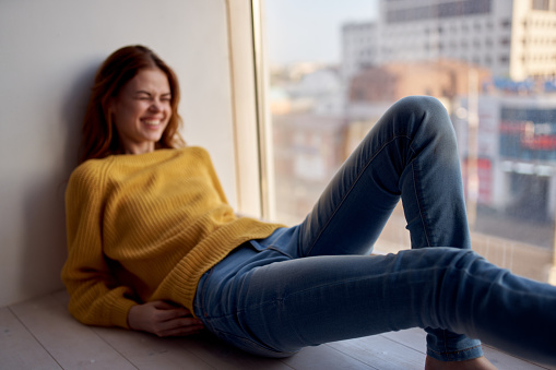 a pretty woman in a yellow sweater lies on the windowsill and looks out the window. High quality photo