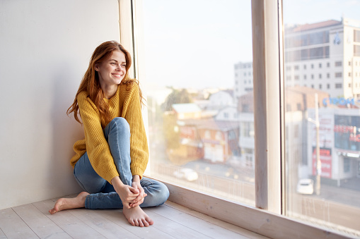 Woman on the windowsill in a yellow sweater and jeans leisure lifestyle. High quality photo