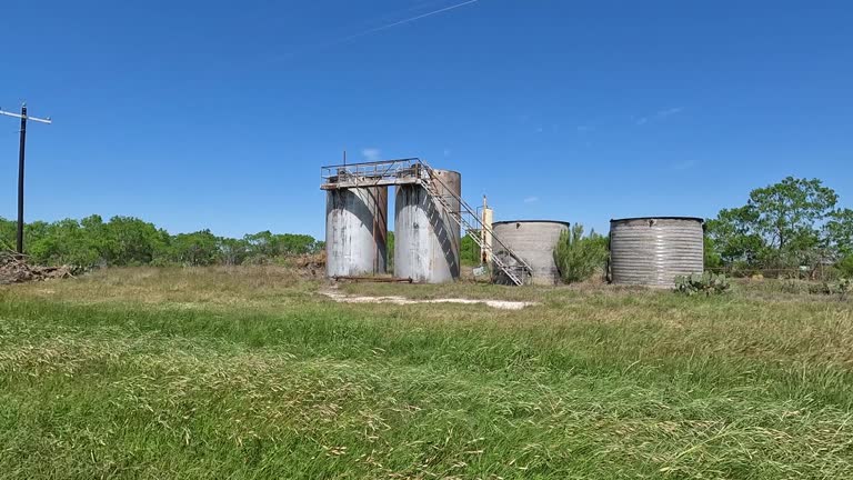 Old oilfield tanks stand in a field on blue sky day near the city of Floresville Texas