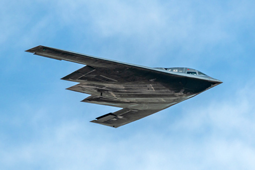 Rapid City, SD – May 14, 2022: A stealth B-2 bomber is in flight against a cloudy sky backdrop, showcasing its distinctive triangular shape and dark color as it passes over the Ellsworth Air Force Base. The aircraft is designed for low visibility on radar, performing what could be a routine exercise or a demonstration.