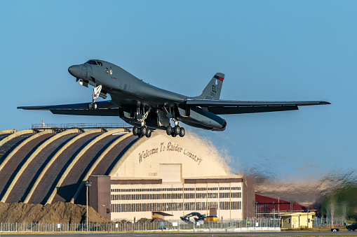 Rapid City, SD – September 27, 2023: A Rockwell B-1B Lancer is departing Ellsworth Air Force Base, showcasing its extended landing gear and intricate underbelly, as it passes the AFB hangar proclaiming Welcome to Raider Country. Raider Country is a reference dating back to the World War II Doolittle Raiders, the predecessor squadron to today’s B-1s.  The B-1B's design, with swept-back wings is designed for long-range missions and high-speed flying.