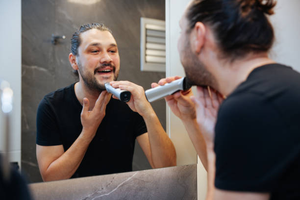 istock A man is using electric shaver to trim mustache and beard while standing in front of mirror in bathroom at home. 2138637187