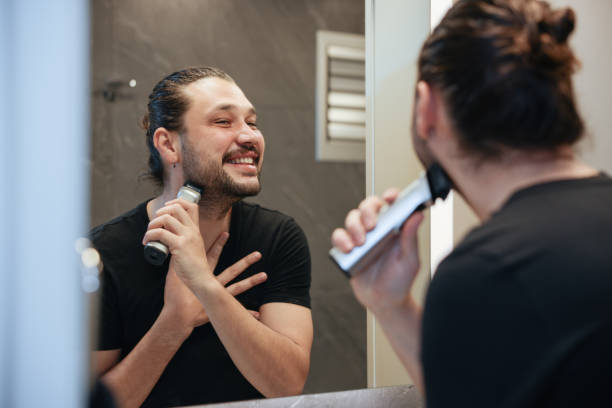 istock A man is using electric shaver to trim mustache and beard while standing in front of mirror in bathroom at home. 2138644545