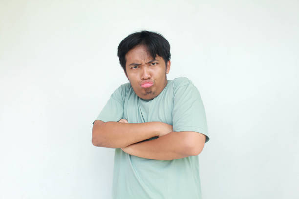 A young Asian man in a green t-shirt with an angry and annoyed expression. Isolated in gray background