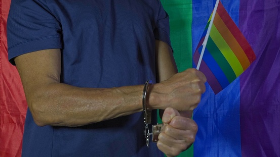 Small rainbow flag in hand, closed fist and handcuffs on wrists. Civil rights and LGBT pride concept