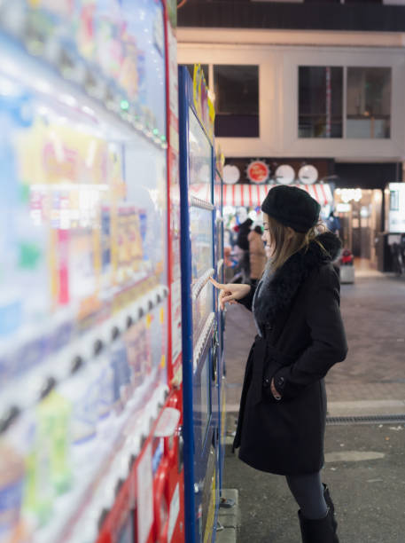 Tourist buying drinks from vending machine at market street night, Osaka city, Japan.