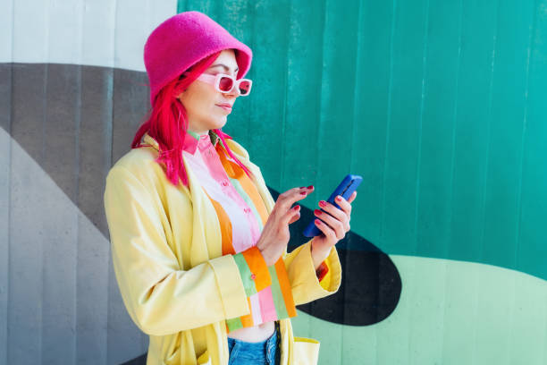 istock Stylish young woman using her phone for messaging, communication or content creating for social media standing on graffiti wall background. Bright hipster street fashion. Influencer, blogger. 2138706325