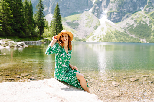 Beautiful woman in green dress enjoys on a mountains on sunny day. Fashion, beauty, lifestyle, travel concept.