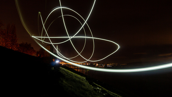 Nighttime scenery with long exposure drawing with light creating shapes a colours with city lights in the background.