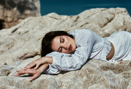 A beautiful woman in a white dress lying on the rocks in beautiful sunny weather.