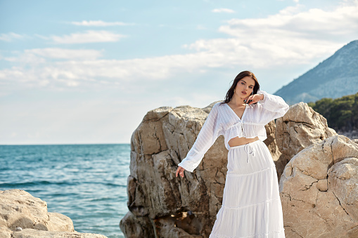A beautiful woman in a white dress standing in front of the rocks.