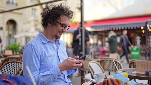 Businessman Texting On His Phone During Breakfast In A Sidewalk Café In Paris, France