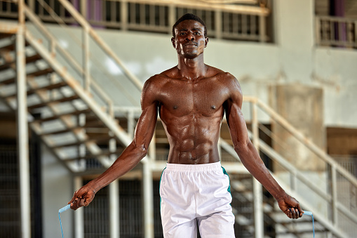 Black young sportsman working out with jumping rope outdoors.