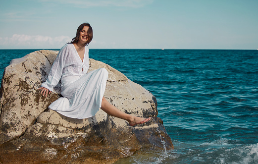 young woman looking playful at sea water in summer holiday enjoying vacation relaxed wearing white beach dress admiring the beauty of the ocean horizon with arms open i freedom concept