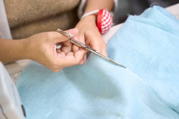 Craftswoman cuts blue fabric with scissors, the workplace is well lit