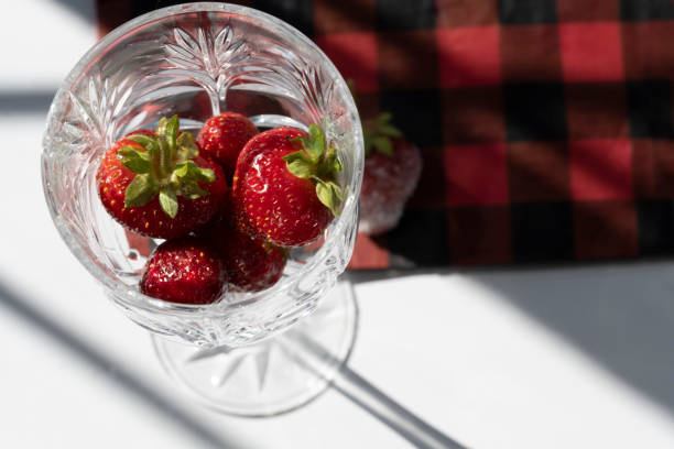 Freshly washed strawberries are placed in crystal glassware showing a plaid napkin on a white background.