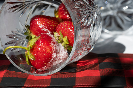 Freshly washed strawberries are placed in crystal glassware showing a plaid napkin on a white background.