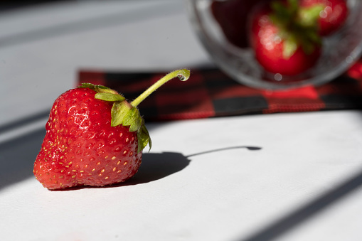 Focus on one main strawberry with a plaid napkin and more berries blurred in the background.