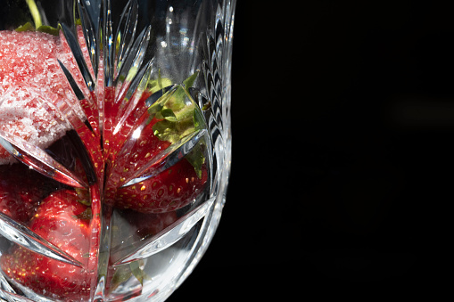 Freshly washed strawberries are placed in crystal glassware on a black background.