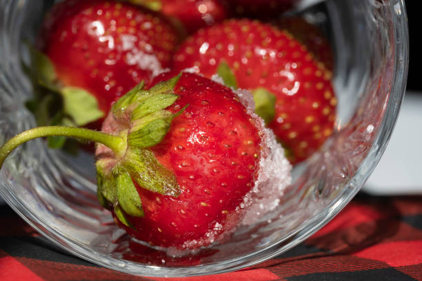 Freshly washed strawberries are placed in crystal glassware showing a plaid napkin on a white background.