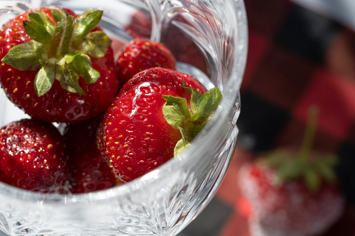 Freshly washed strawberries are placed in crystal glassware with a plaid napkin in the background.