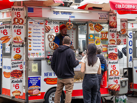 New York City, USA - March 2024: Customers purchasing lunch from a food truck on the street. Fast, inexpensive food in the city for busy people. Small business vendor.
