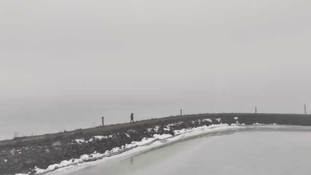 A person walking a path along a pier on a misty winter day