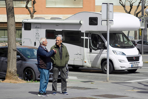 Tarragona, Spain - April 4, 2024: On a sunny day in Tarragona, two people stop to chat near a white caravan, capturing an everyday moment.