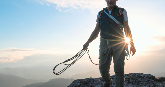 Mature climber stands on mountain top with rope at sunset