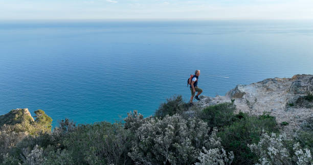 istock Mature man ascends rock ridge crest above sea 2138868397