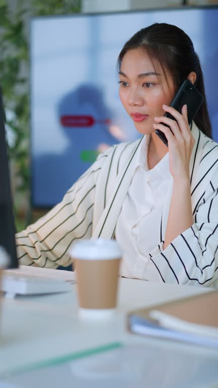 Female professional is with laptop sitting at table.Thoughtful Businesswomaman discussion with a business partner via smartphone while checking finacial annual report on computer screendaylight in a modern office. Business Communication with technology