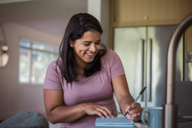 istock Multiracial pregnant woman smiles while writing in notebook 2138893367