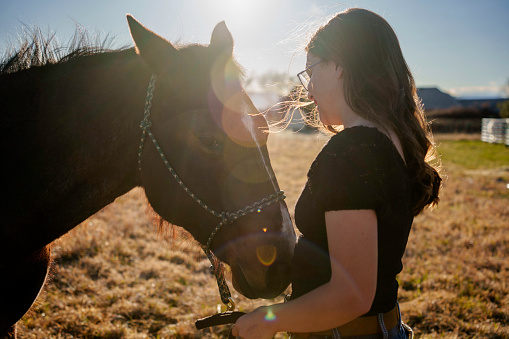 Pretty Young Caucasian Woman Smiling with Her Quarter Horse with Hazy Light in a Grassy Field at Sunset