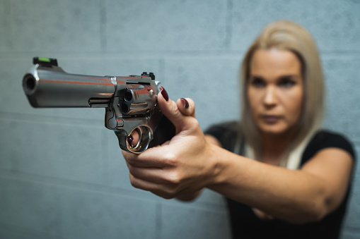 A girl takes aim with a chrome-plated revolver, soft focus photo. Close up photo