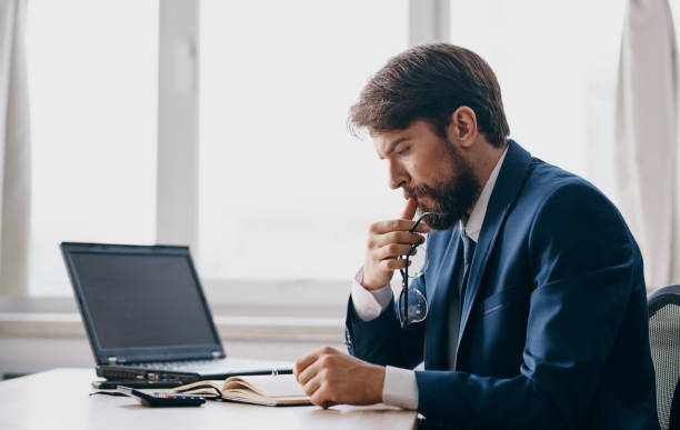 istock A man in a classic suit sits at a table and an open laptop office window a puzzled look 2138942132