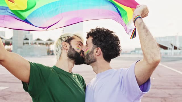 Gay couple kissing in love as they celebrate LGBT Pride Day parade with a rainbow flag