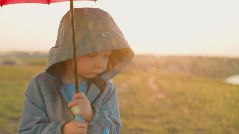 Sad boy clutches umbrella tightly in field