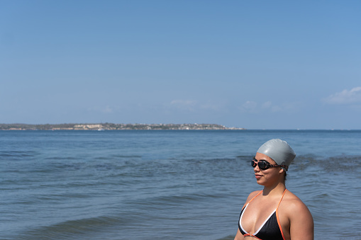 A contemplative swimmer in cap and sunglasses stands by the tranquil sea.