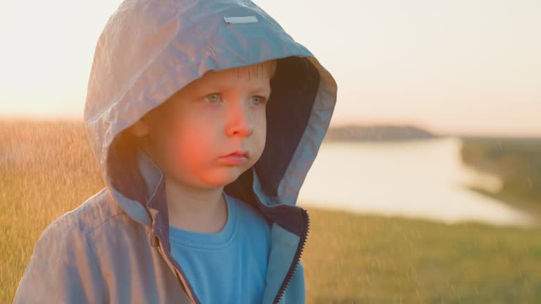 Offended child under rain on riverbank