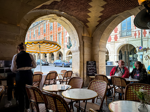 Paris, France - 20.02.2024. View of Cafe Hugo at Place des Vosges in Paris. Charming view from vaulted arcade. Spring in Paris. Popular touristic Brasserie.
