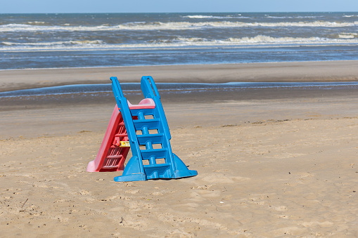 A plastic playground slide on the beach of the North Sea in the sun in front of a rough sea